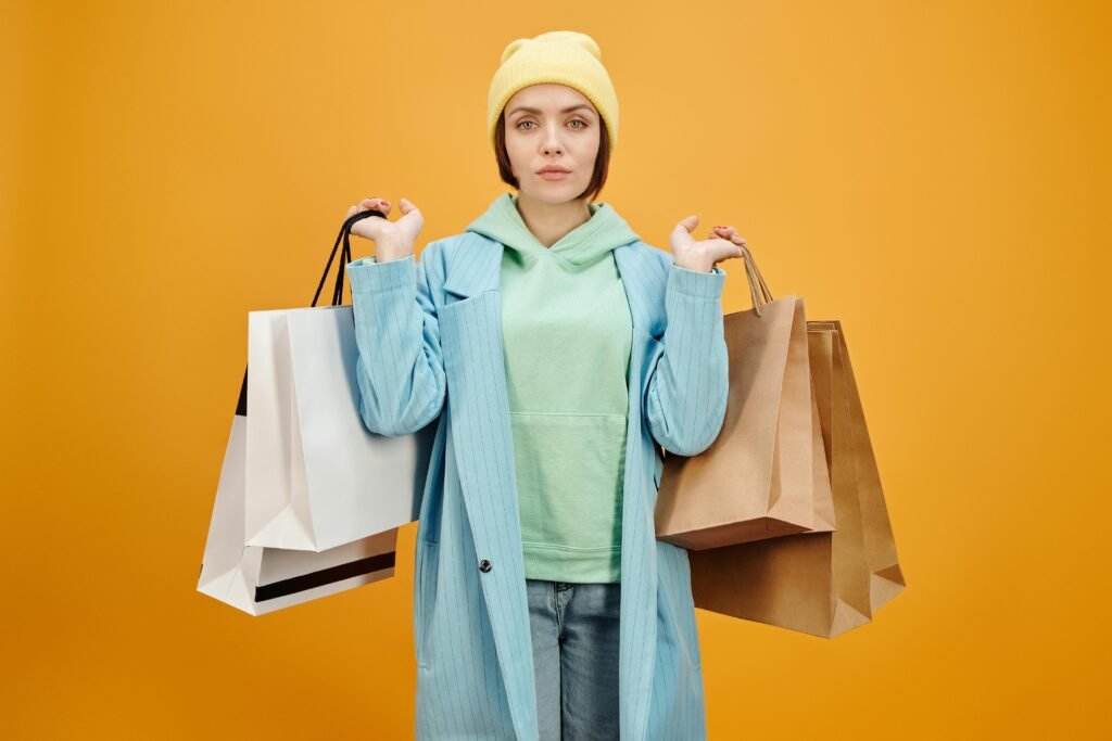 Stylish woman in colorful outfit holding multiple shopping bags against a vibrant yellow background.